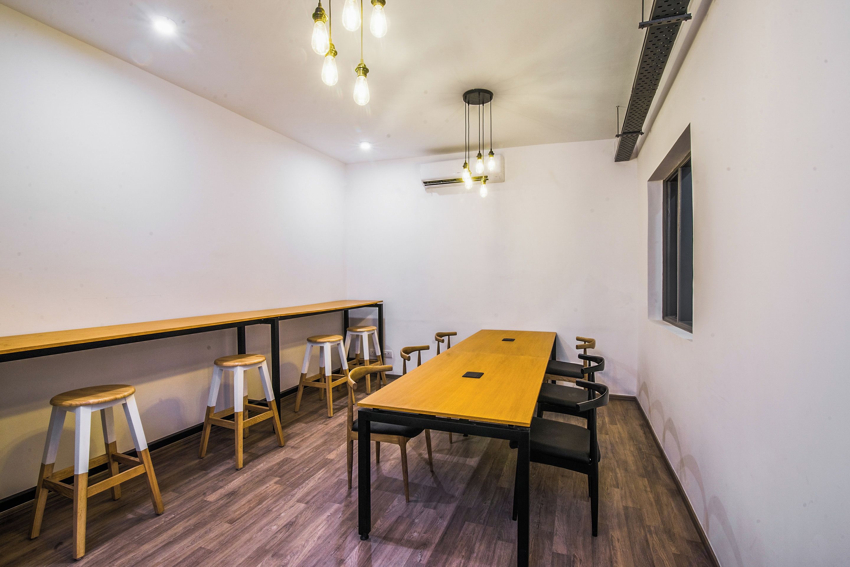 A conference room with a long table, four stools, and hanging pendant lights.