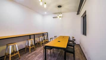 A conference room with a long table, four stools, and hanging pendant lights.