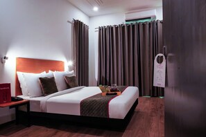 Quarto de hotel com cama, mesa de cabeceira e criado-mudo com telefone.