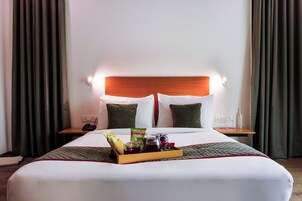 Habitación de hotel con cama, mesita de noche con teléfono, bandeja de aperitivos y una botella de agua.