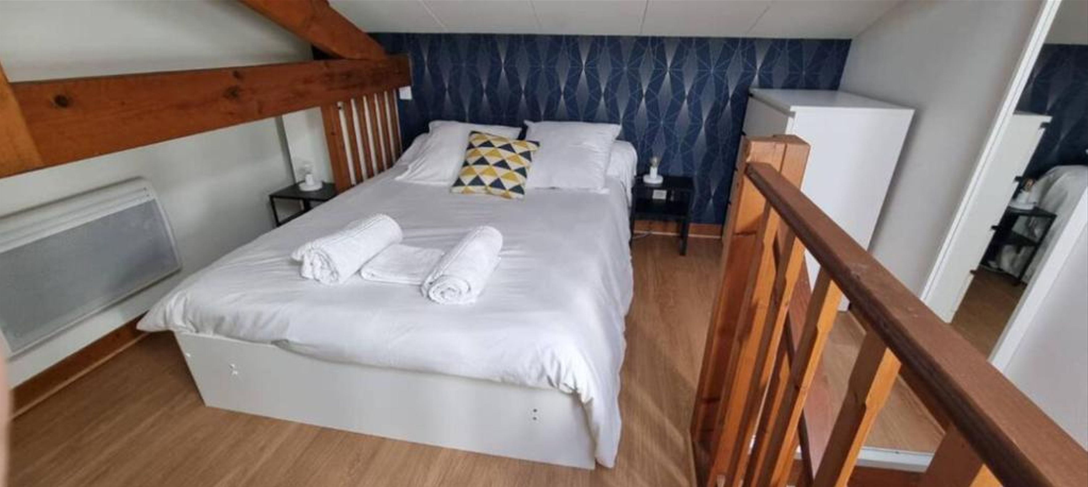 Una habitación de hotel con cama, cabecera de madera, mesita de noche, escritorio y armario.