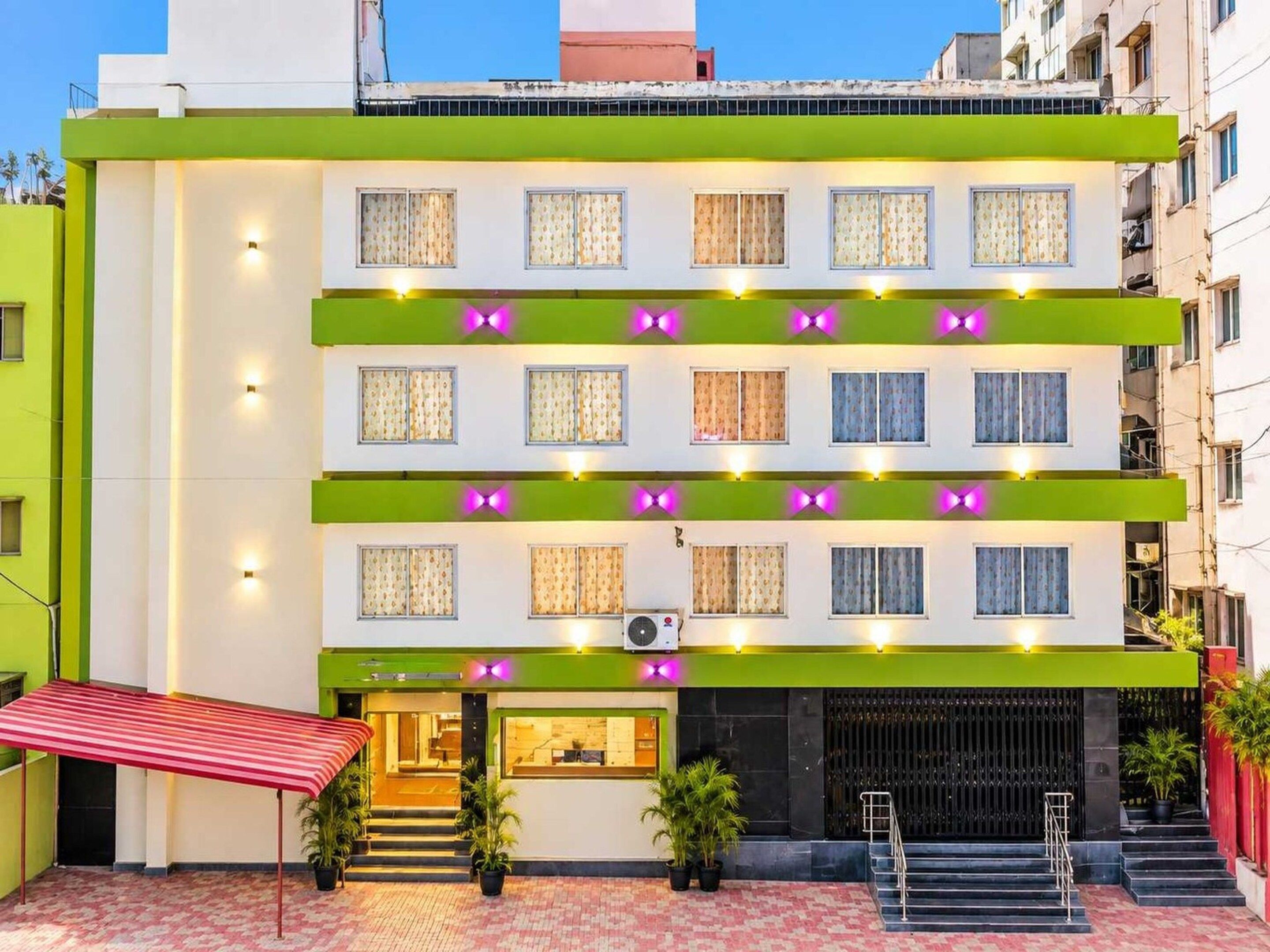 A multi-story hotel with a green facade, multiple windows, and a staircase leading to the entrance.