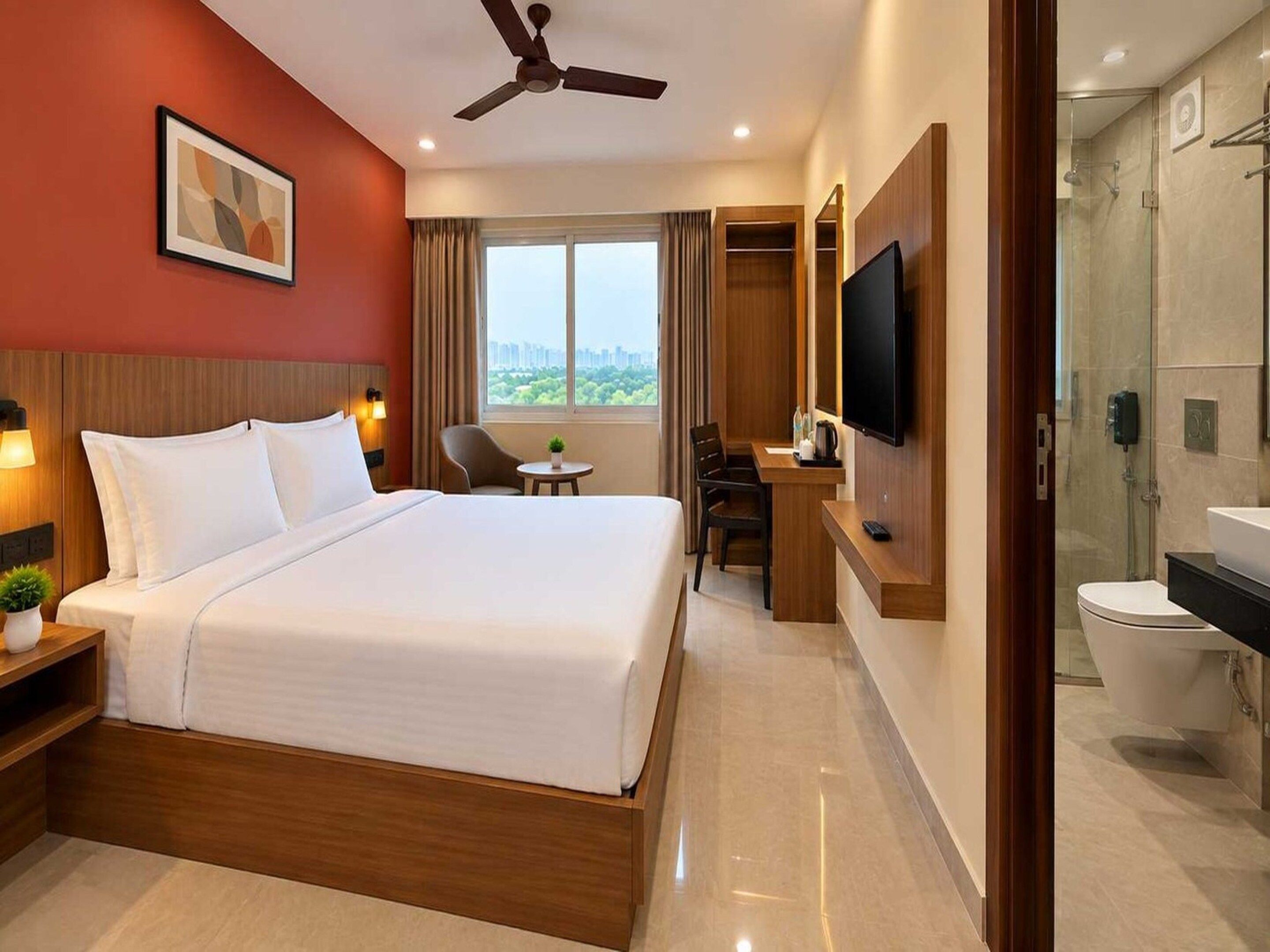 A hotel room with a bed, desk, chair, TV, and a bathroom with a toilet and shower.