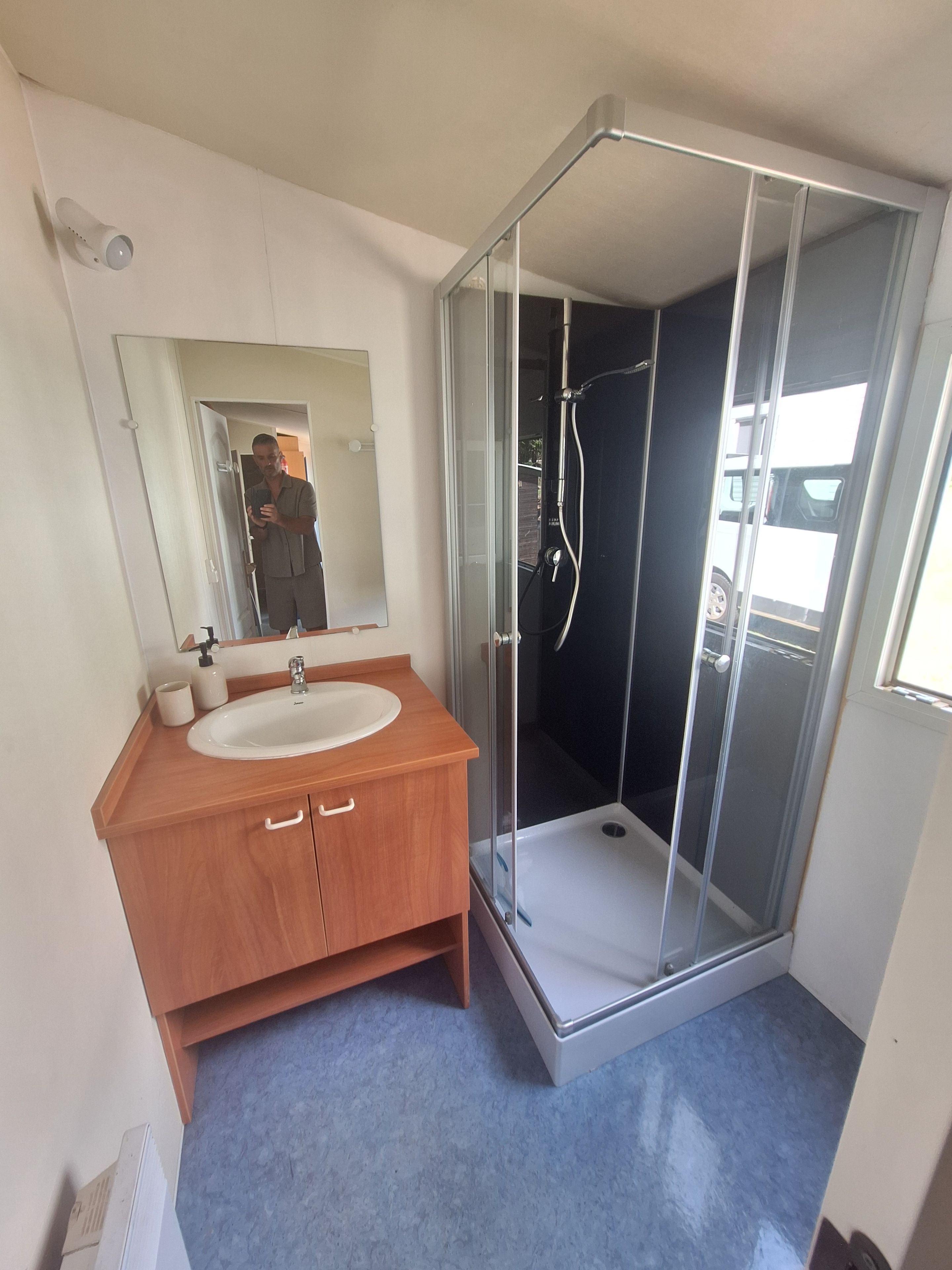 A bathroom with a wooden vanity, a white sink, a mirror, and a glass-enclosed shower.