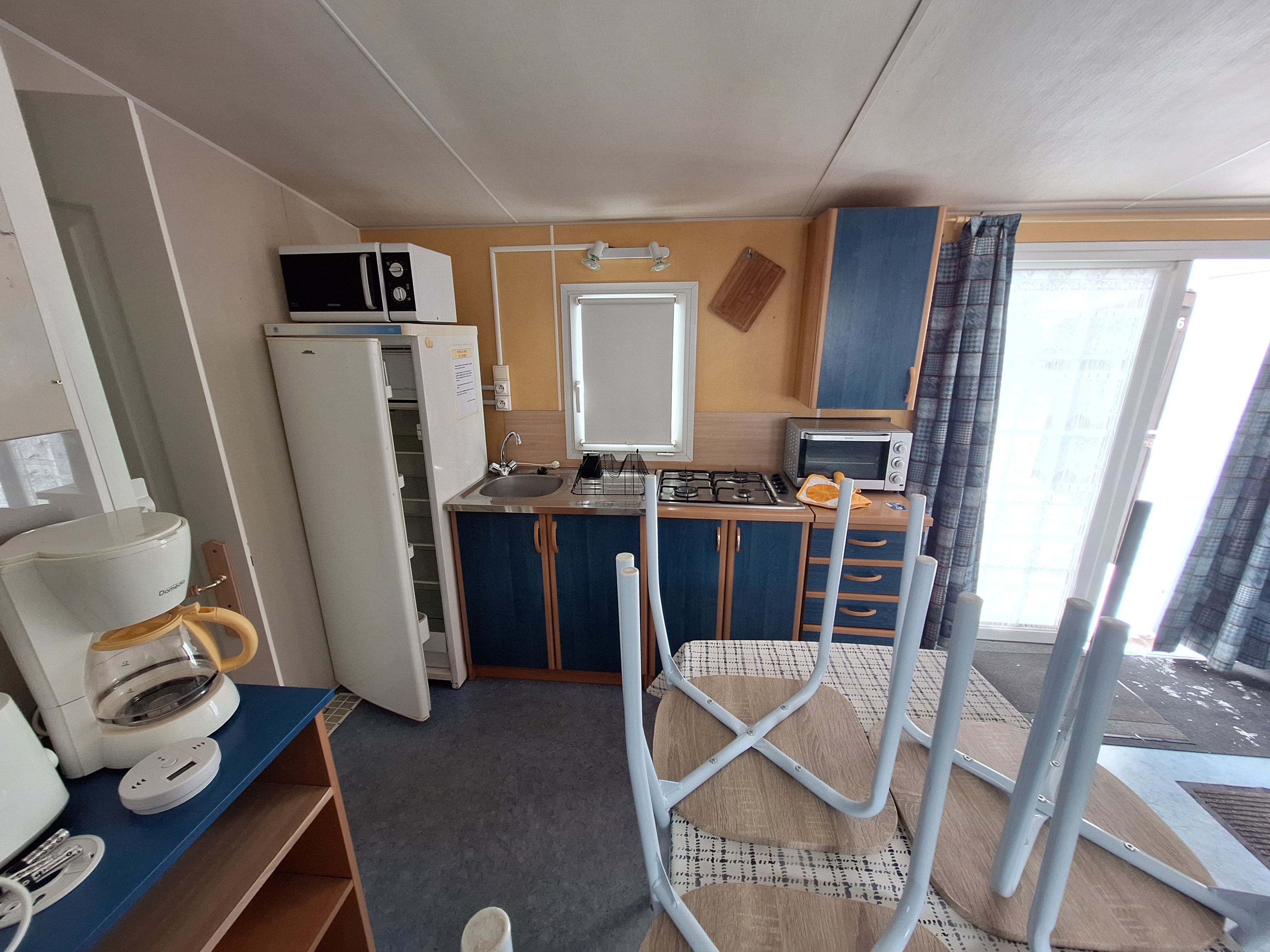 Une petite cuisine équipée d’un micro-ondes, d’un réfrigérateur et d’une cuisinière. Un petit coin repas est aménagé avec une chaise et une table.