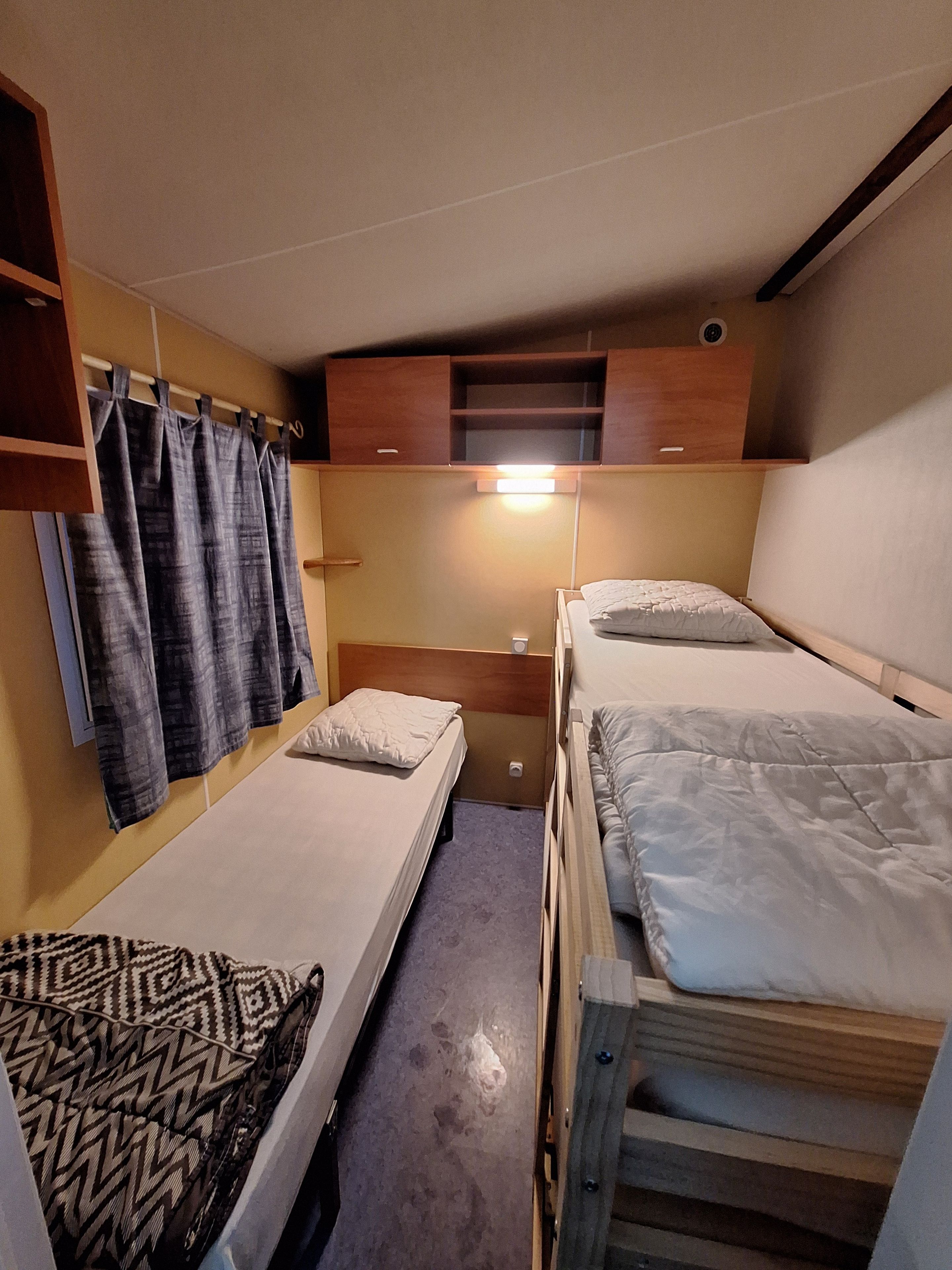 Habitación pequeña con dos literas, un escritorio y una cortina.