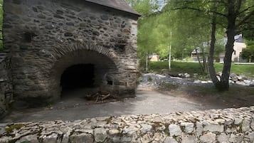 En byggnad av sten med en välvd entré, omgiven av grönska och en stenmur.
