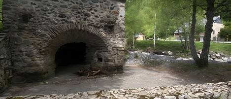 A stone building with an arched entrance, surrounded by greenery and a stone wall.