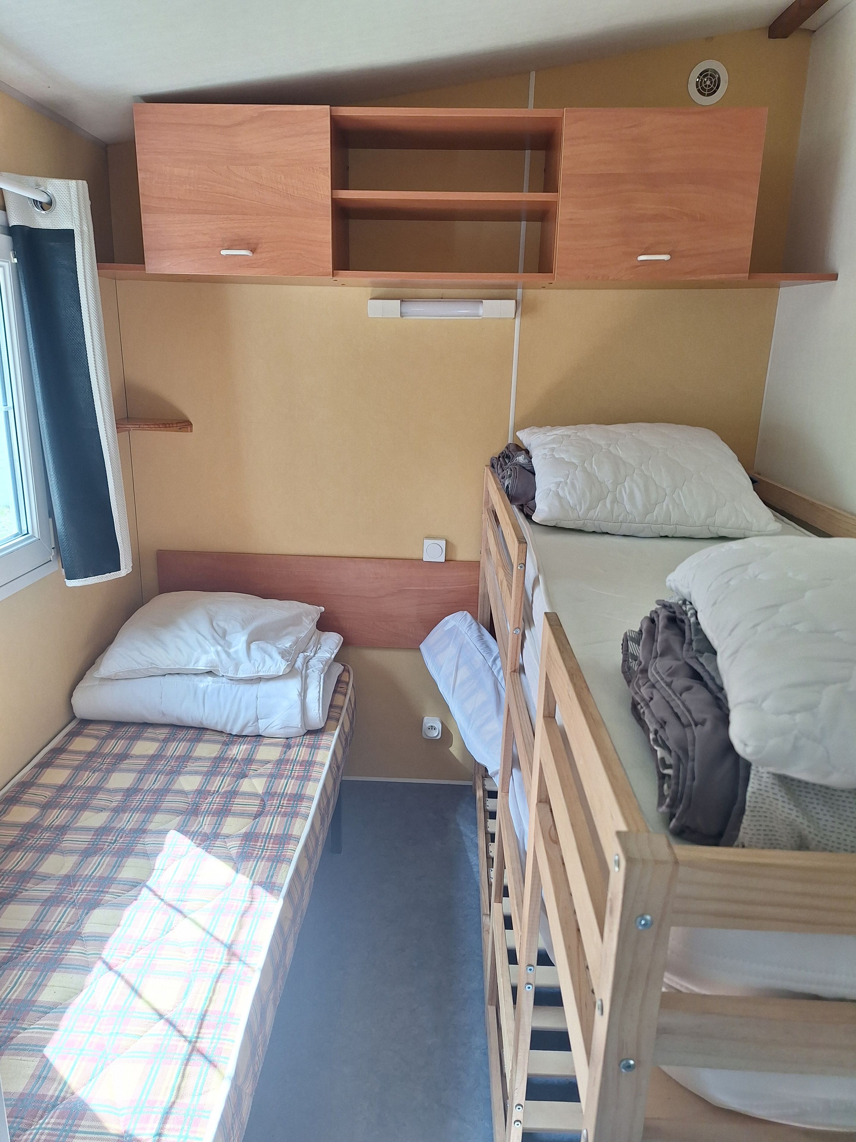 Habitación pequeña con una cama litera, un escritorio y silla, una ventana con cortina y un estante en la pared.