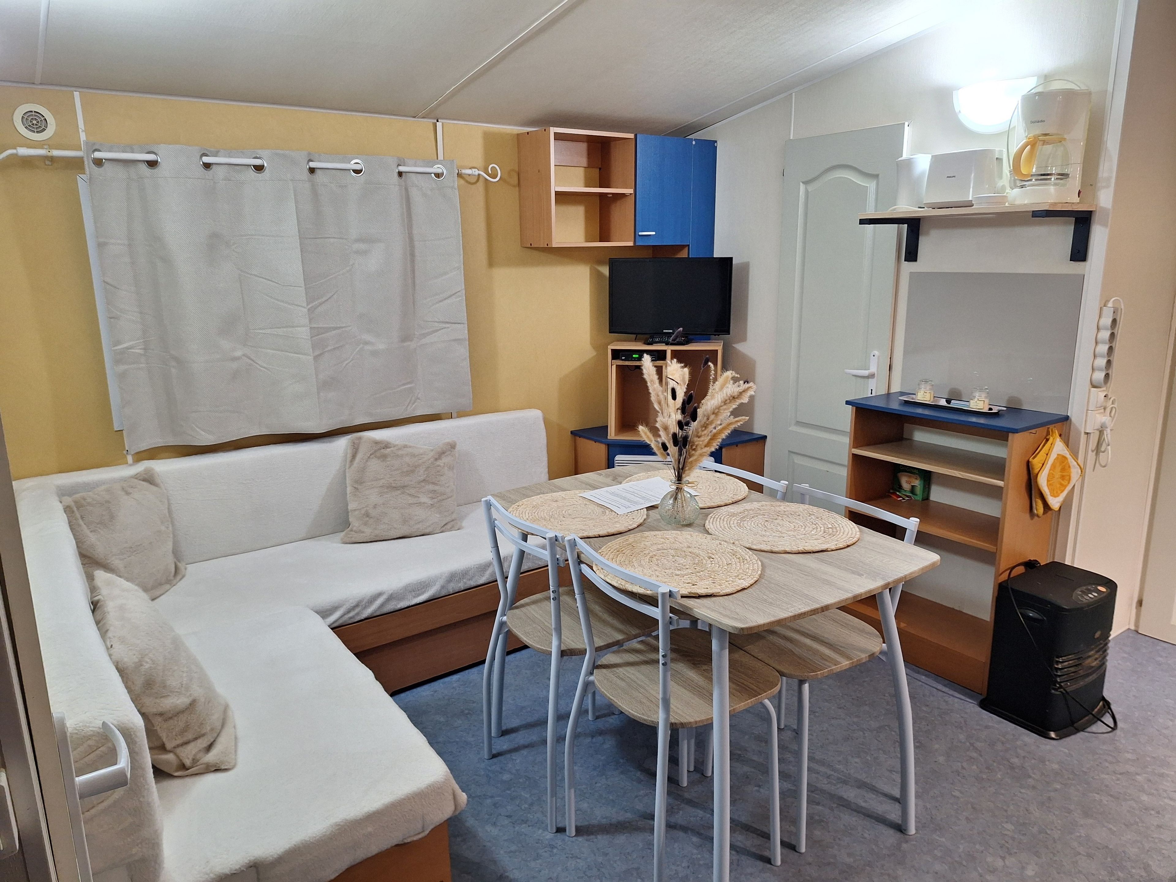 En kompakt opholdsstue med sofa, spisebord med servietter, fjernsyn og et tekøkken.