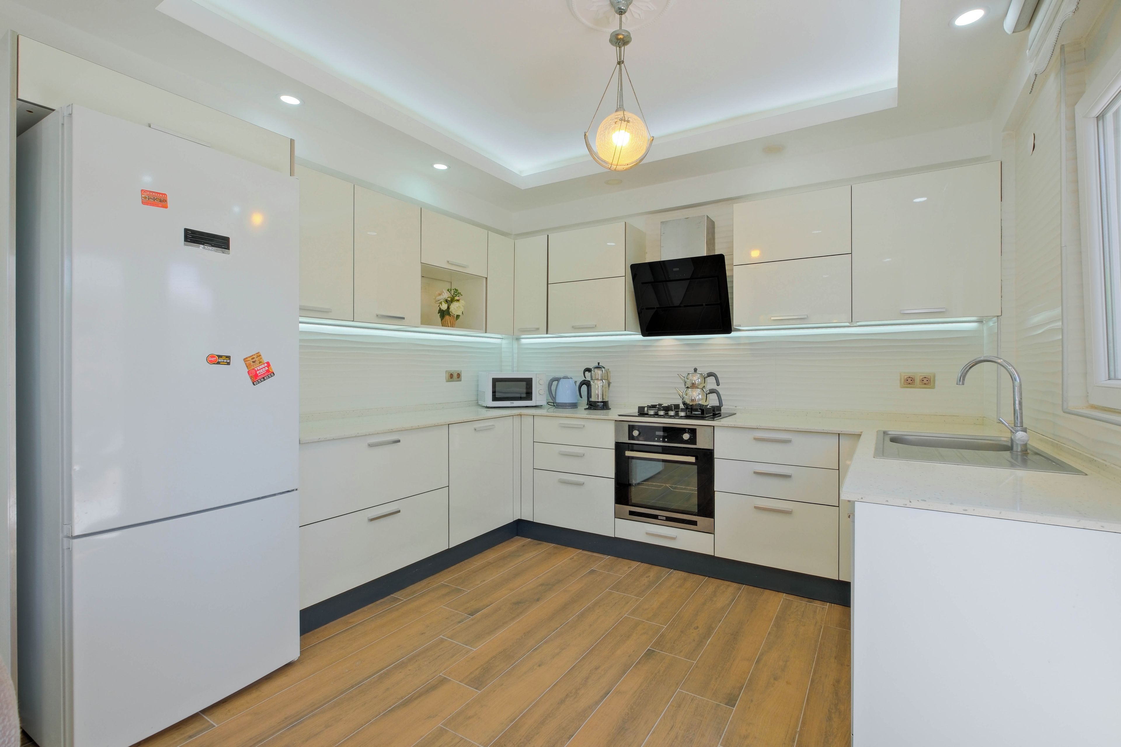 A modern kitchen with white cabinetry, a built-in oven, a microwave, and a hanging light fixture.