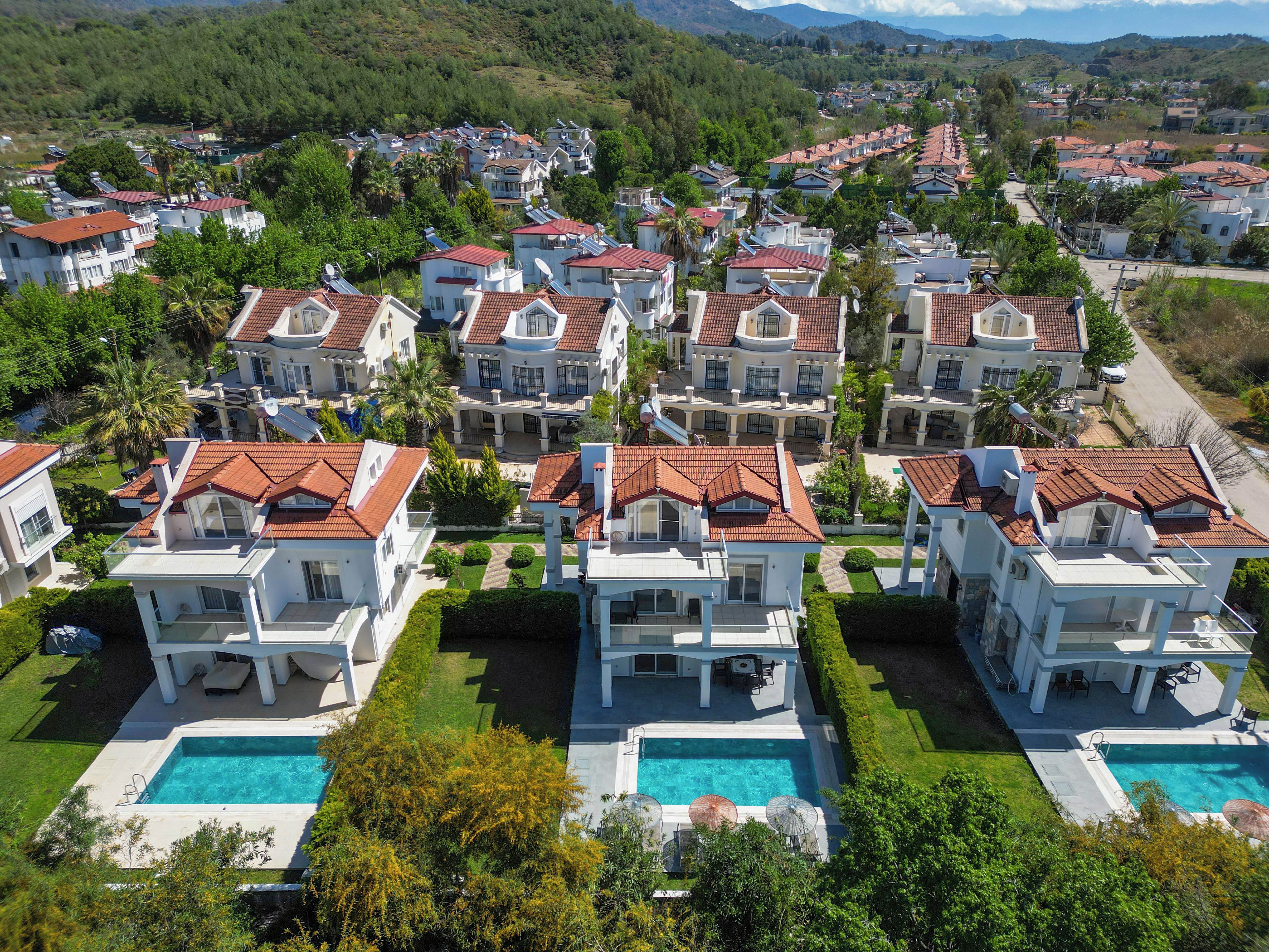 A residential area with multiple houses featuring red-tiled roofs, a swimming pool, and lush greenery.