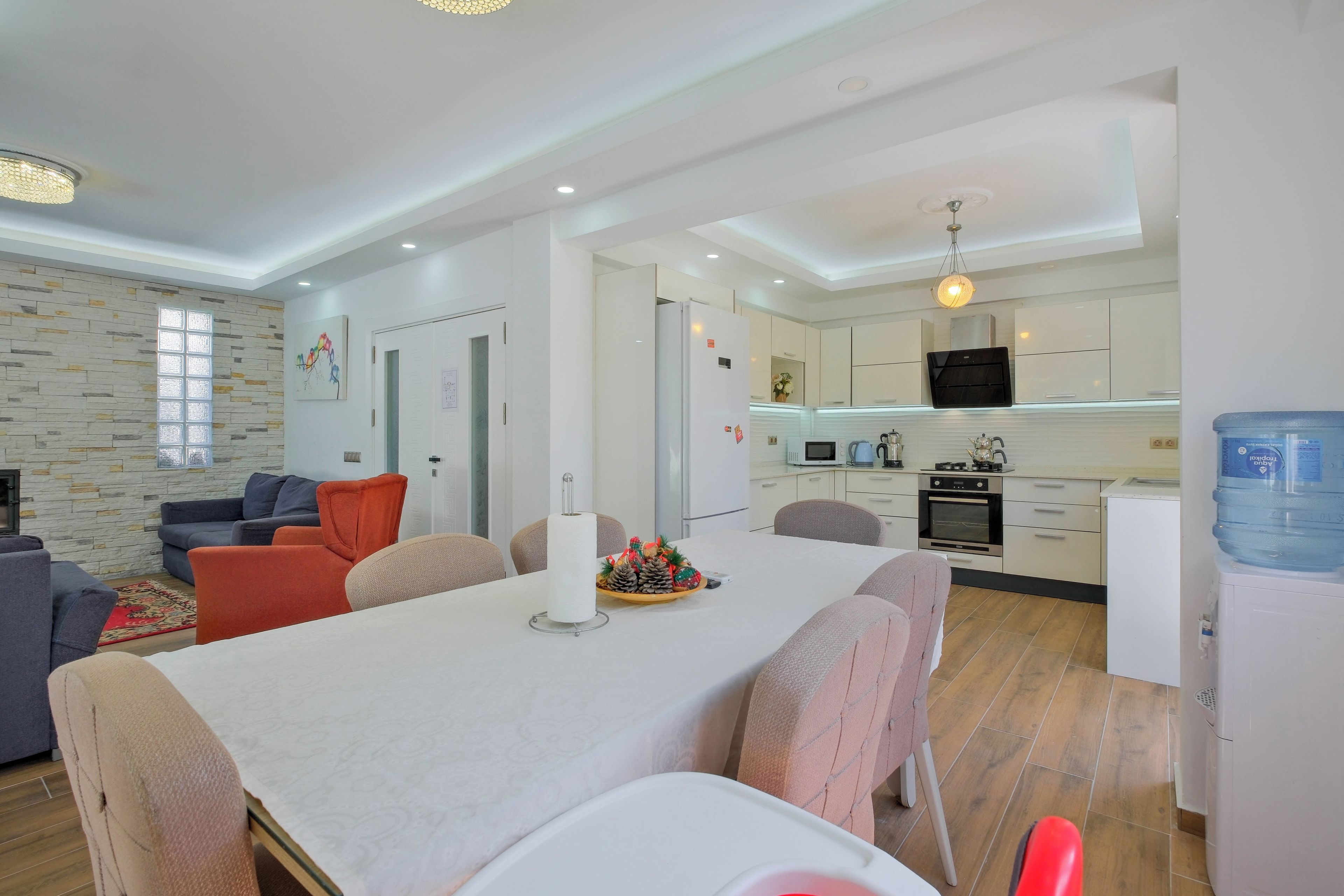 Een moderne woonkamer met een eettafel, banken en een keuken met apparatuur.