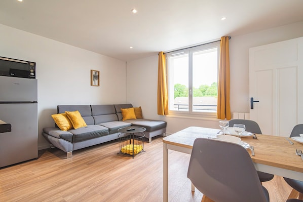 A modern living space with a sofa, dining table, and a kitchen area.