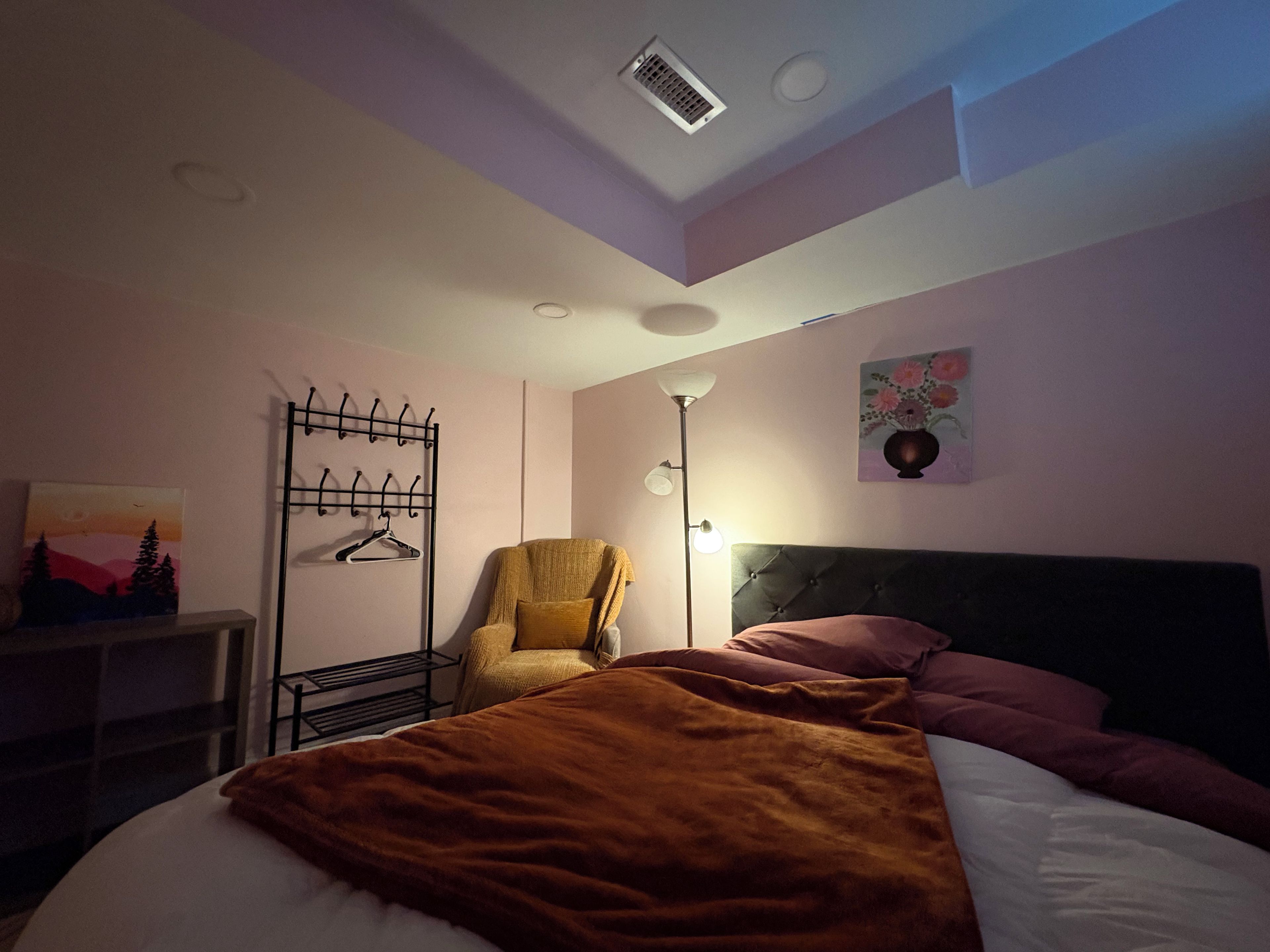 A bedroom with a bed, a chair, a coat rack, and a painting on the wall.