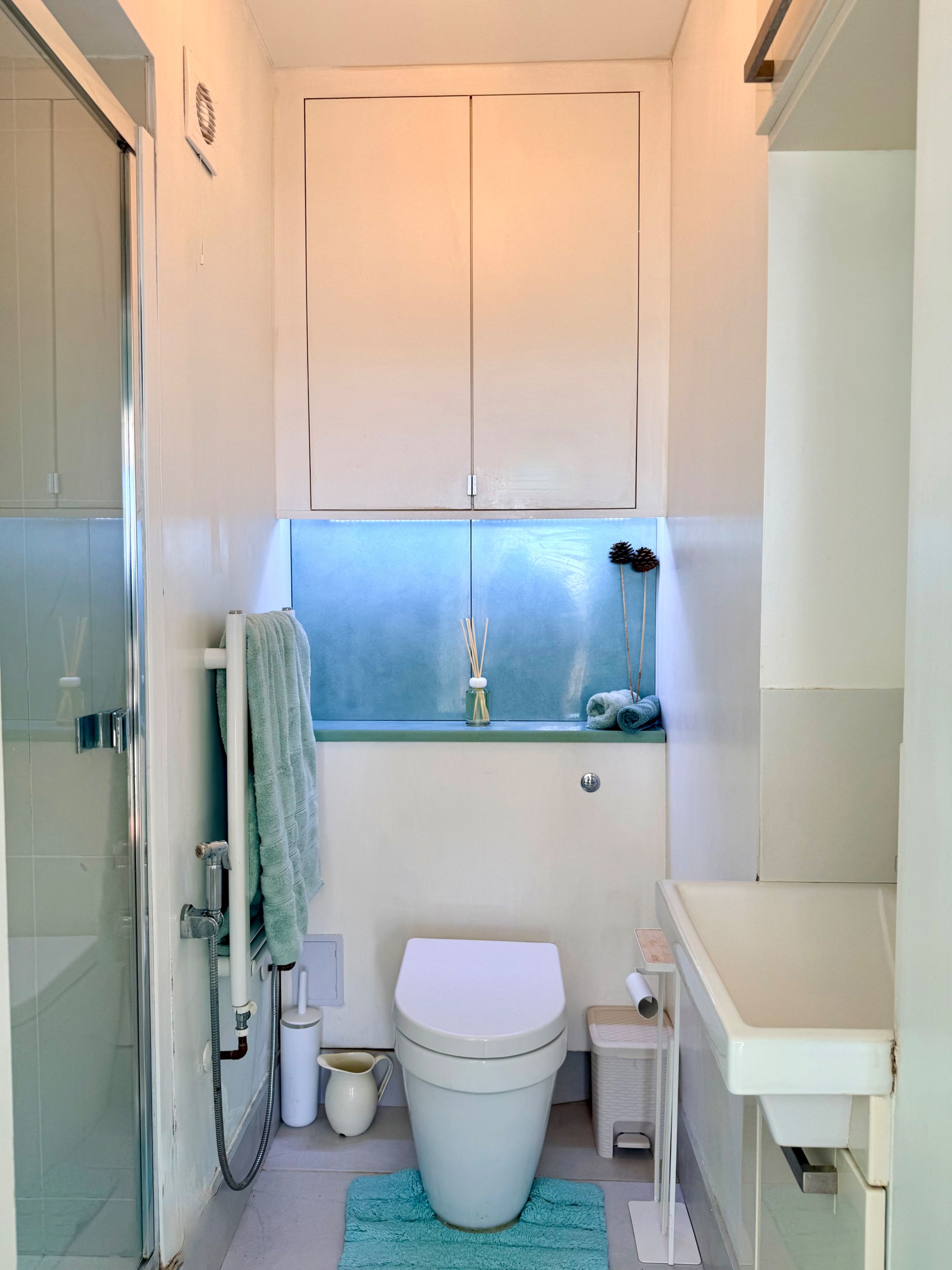 Un baño pequeño y funcional con inodoro, lavamanos, ventana y zona de ducha.