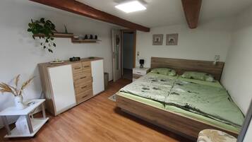 A bedroom with a wooden bed, a desk, a wardrobe, a nightstand, and a wall-mounted shelf with decorative items.
