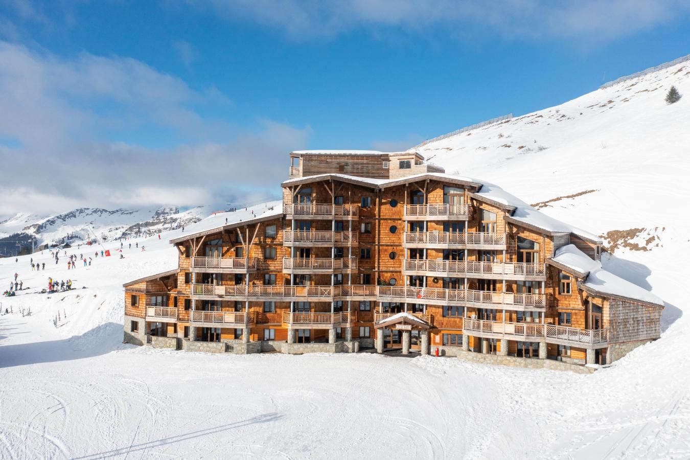 Een meerlaags houten lodge met balkons, gelegen tegen een besneeuwde berg op de achtergrond.