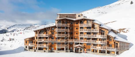 A multi-story wooden lodge with balconies, set against a snowy mountain backdrop.