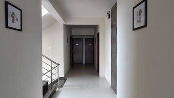 A hallway with a staircase on the left, two doors at the end, and framed pictures on the walls.
