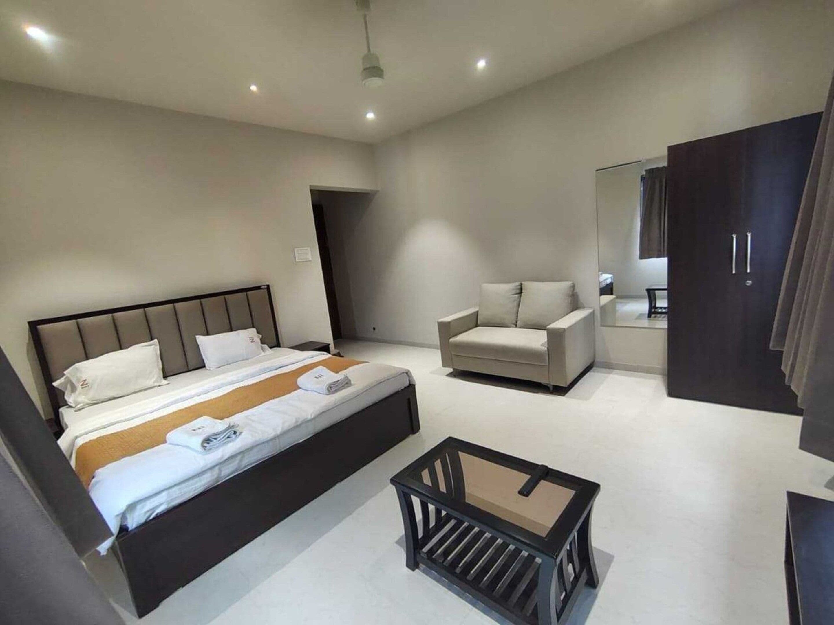 A modern hotel room with a bed, a sofa, a small table, and a wardrobe.