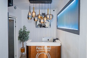Een receptiebalie met een logo, een kamerplant en een moderne kroonluchter.