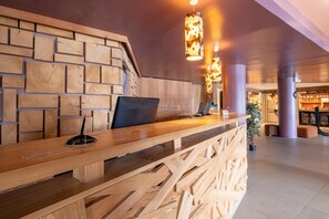 Ein Empfangstresen mit einem Laptop, eine Holzwand mit Backsteinmuster und hängende Pendelleuchten.