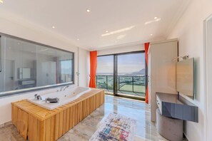 A modern bathroom with a large bathtub, a glass shower enclosure, and a view of the landscape. - zeytintepe villa (Antalya)