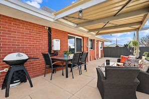 A patio area with a barbecue grill, dining table, chairs, and outdoor furniture. - Eclectic colourful comfortable home, with a cool vibe (Shoalwater)