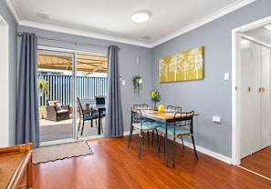 A dining area with a table and chairs, a sliding glass door leading to an outdoor patio, and a wall-mounted artwork. - Eclectic colourful comfortable home, with a cool vibe (Shoalwater)