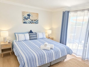 A hotel room with a bed, two bedside tables, a wall-mounted artwork, and a view through a window with curtains. - Eclectic colourful comfortable home, with a cool vibe (Shoalwater)