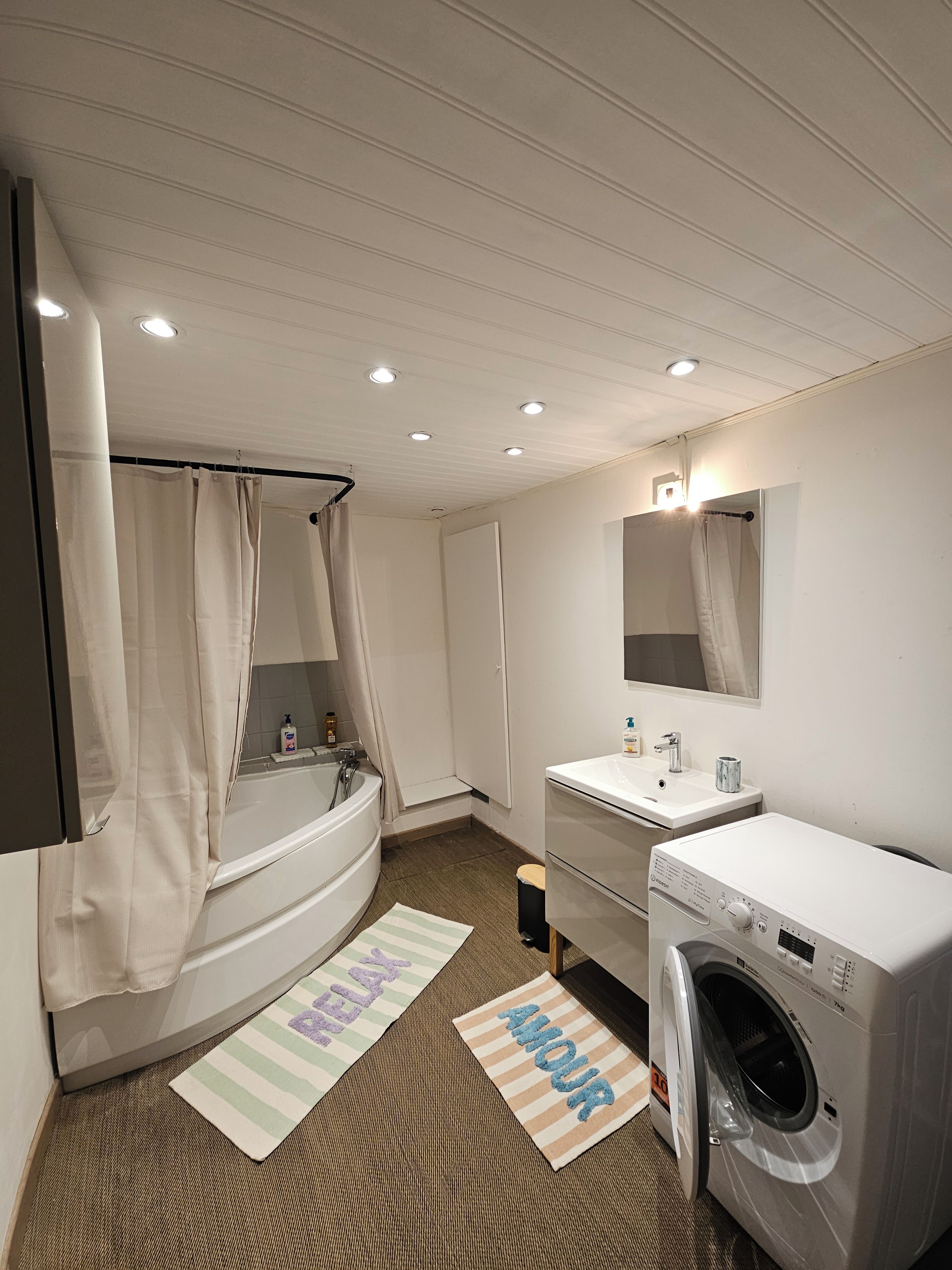 Une salle de bain moderne équipée d’une baignoire, d’un lavabo, d’un miroir, d’une douche et d’un lave-linge.