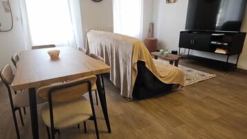 Ein möbliertes Wohnzimmer mit Esstisch, Stühlen, einer Couch, einem Fernseher und einer Uhr an der Wand.