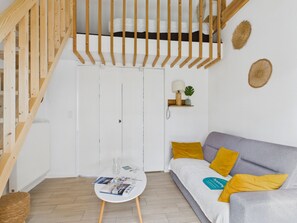 En modern inredning med en trätrappa, en vit soffa med gula kuddar, ett litet bord med tidningar och en vägghylla med en lampa och en växt.