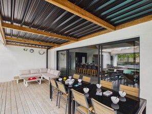 An outdoor dining area with a glass table and chairs, a wooden deck, and a modern interior visible through the glass doors. - Studio for 4, heated pool & shared garden (Saint-Alban)
