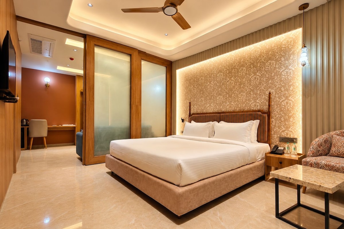 A modern hotel room with a large bed, a desk, a chair, and a small table.