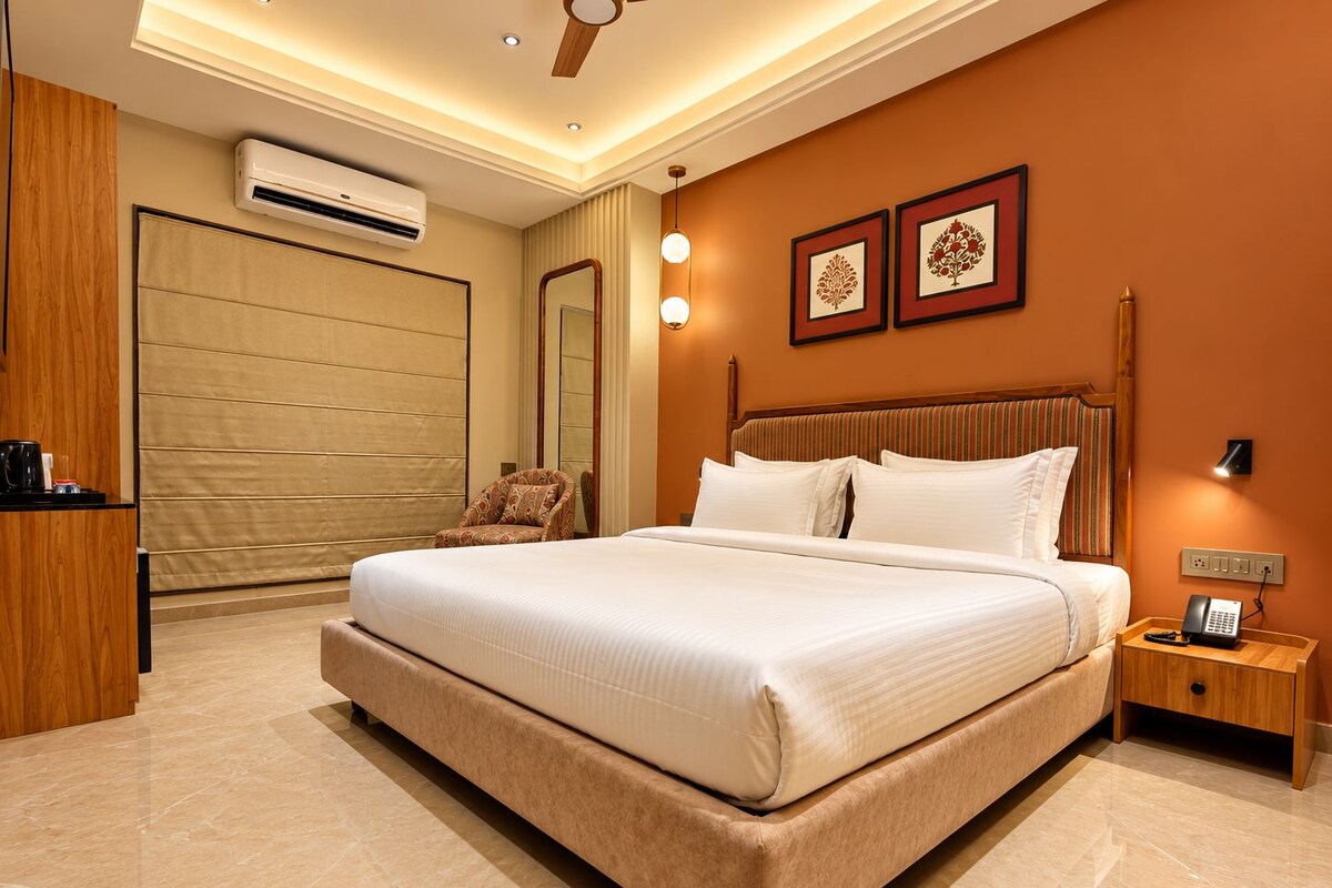 A modern hotel room with a large bed, a bedside table with a phone, a wall-mounted air conditioner, and a ceiling fan.