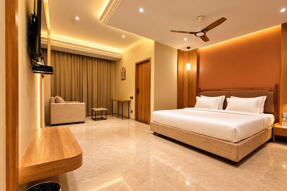 A hotel room with a bed, a sofa, a small table, a ceiling fan, and a trash bin.