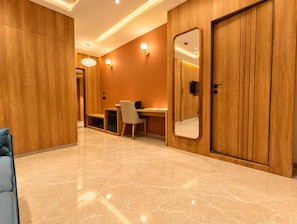 A hotel room with a wooden wardrobe, a desk with a chair, a mirror, and a bed.