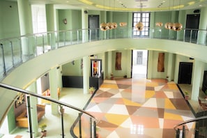 Un interior de varios niveles con un espacio central abierto, barandillas de vidrio y un suelo de patrón geométrico.