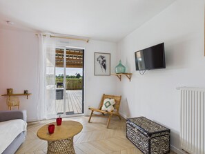 A room with a bed, a round table with red cups, a wicker chair, a television on the wall, and a view through a glass door to an outdoor deck. - Studio for 2, heated pool & shared garden (Saint-Alban)