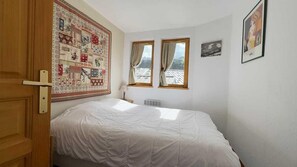 A bedroom with a bed, two windows, a radiator, and a door. - Ski-in/ski-out & foot of the slopes, 2nd floor, balcony, tv, 31m², Courchevel (Courchevel)