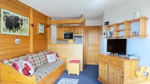 A cozy cabin interior with a wooden sofa, a television, and a kitchen area. - Ski-in/ski-out & foot of the slopes, 2nd floor, balcony, tv, 31m², Courchevel (Courchevel)