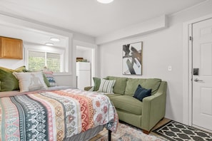 A bedroom with a bed, a green sofa, a window with blinds, a door, and a wall-mounted artwork. - Cozy Studio • Prime Location • Fast WiFi & Parking (Billings)