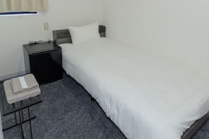 A single bed with a white mattress and a grey headboard, a bedside table with a lamp, and a folded towel on a small table. - HOTEL GINZA Plus (Imabari-shi Tokiwacho)