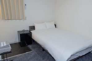 A hotel room with a bed, a nightstand, a lamp, a window with blinds, and a small table with a towel. - HOTEL GINZA Plus (Imabari-shi Tokiwacho)