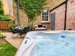 Un jacuzzi en un patio trasero con una pared de ladrillo, una ventana y mobiliario exterior.