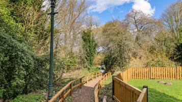 A wooden pathway leading to a bridge over a stream, surrounded by trees and a wooden fence.