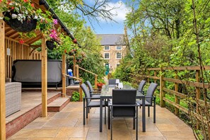 Un patio al aire libre con mesa y sillas, una parrilla y cestas de flores colgantes.