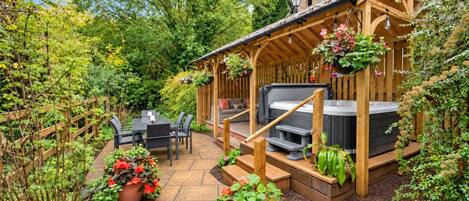 A patio area with a wooden pergola, outdoor seating, and a hot tub.